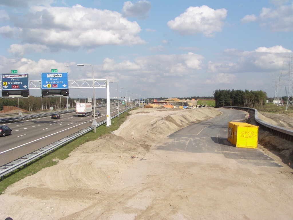 p4120129.jpg - Overzicht Kp. Leenderheide vanaf de Roostenlaan. Links de A67 met nu nog rechtsaffer naar de A2 richting Maastricht. Dat draait dus om: voor de richting Venlo is het dadelijk uitvoegen en onder KW 33 (enigzins zichtbaar in het midden) door, dan terug omhoog naar de bestaande A67 viaducten over de rotonde. De parallelbaan rechts gaat eveneens onder KW 33 door maar eindigt op de rotonde.