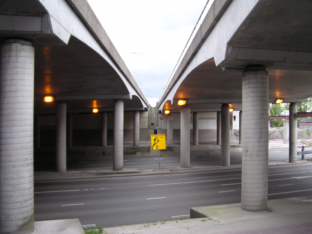 p4300036.jpg - Viaduct (rechts) waarover de toerit in de richting Maastricht een beperkt aantal jaren overheen heeft gelegen, loopt taps toe naar de hoofdrijbaan. Bij het verbreden ervan tot parallelbaan blijft die vorm gehandhaafd. De parallelbaan gaat er dan ook enigzins scheef overheen lopen.
