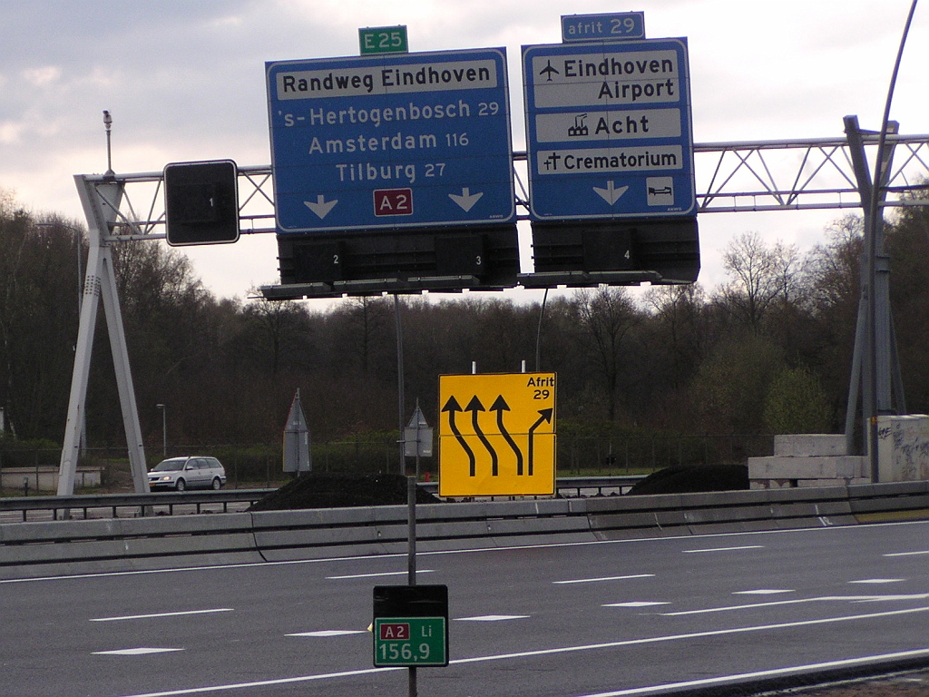 p4050010.jpg - Laten we eens stilstaan bij het lot van het linker portaalbord. Op deze foto uit april 2008 is het sinds kort werkeloos, maar hangt er nog in zijn oude glorie. Het monumentale aangelichte paneel heeft er vele trouwe dienstjaren opzitten in de autosnelwegbewegwijzering op de A2 Eindhoven. Als eerste stap in een langdurig gedwongen aftakelingsproces werd het zijn aanlichtarmaturen ontnomen, en gedegradeerd tot  tijdelijk bord boven de parallelrijbaan . Het moest daar ook nog een autowegbordje naast zich dulden met nieuwerwetse dwalingen zoals omhoogwijzende pijlen.