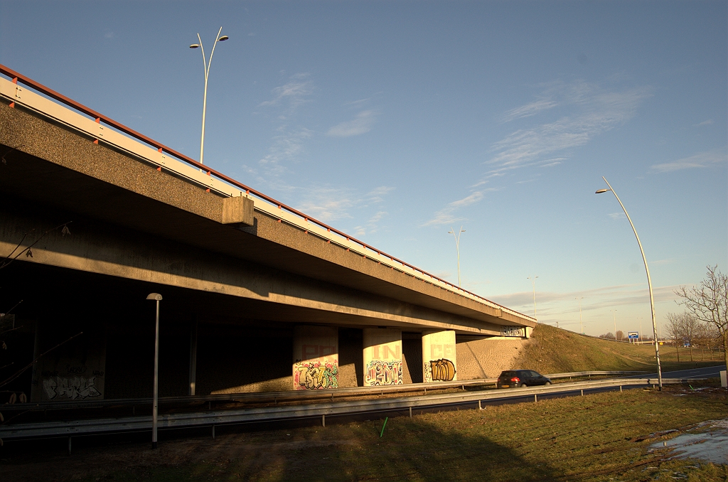 20091226-161709.bmp - Kp. Ekkersweijer valt eigenlijk buiten het project, maar toch is hier werk gaande. Enkele voorheen onverlichte verbindingswegen in het knooppunt zijn voorzien van de typerende lichtmasten model "Randweg Eindhoven", zoals hier op de voorgrond langs de verbindingsweg Amsterdam-Nijmegen in de A2. Het viaduct in de A50/8 heeft betonnen aanhangsels voor lichtmasten, waarvan we eigenlijk niet weten of ze ooit benut zijn. Hoe dan ook zijn er nu nieuwe masten in de middenberm geplaatst...
